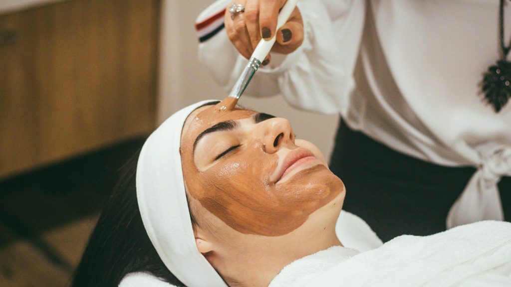 Femeie relaxată, cu ochii închiși, care primește un tratament facial cu mască într-un salon