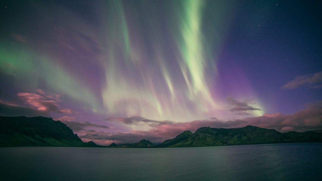 Aurora boreală verde și violet deasupra lacului Álftavatn și a munților din Islanda