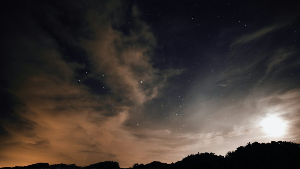 Cer de noapte cu stele și lună luminoasă deasupra unei coaste întunecate